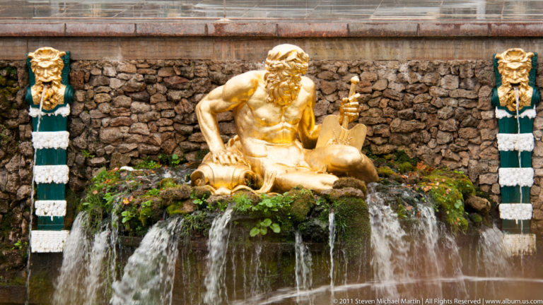 Seated gilded bearded figure in a rocky grotto above falling water, flanked by striped supports and masks.