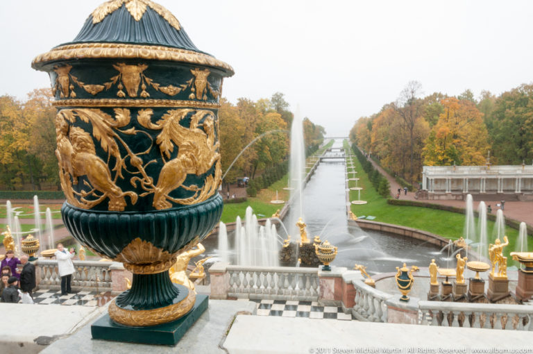 Large black-and-gold ornamental urn in foreground overlooking fountains and the long straight Sea Canal.