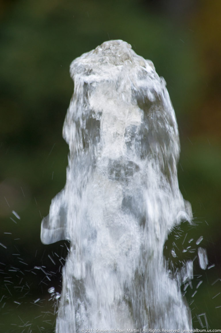 Close-up of churning fountain water forming a rounded translucent surge with droplets spraying outward.