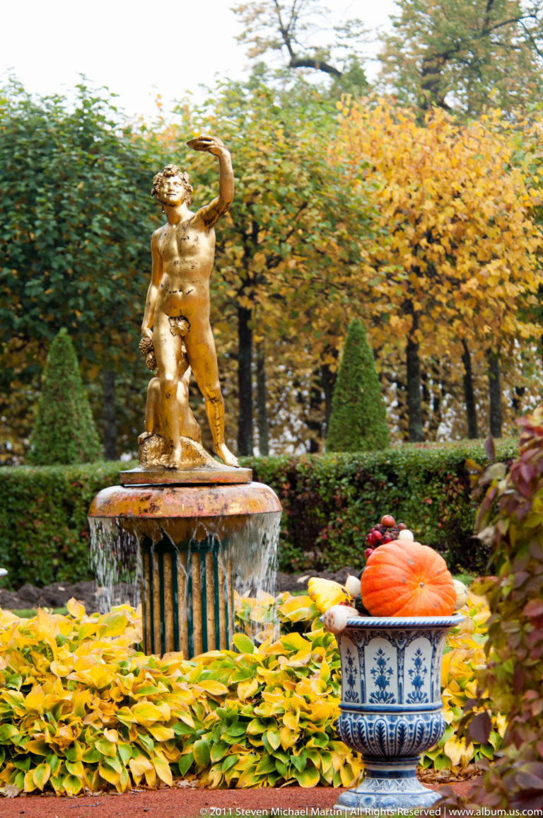 Gilded garden figure above a low fountain with pumpkins and gourds displayed in a blue-and-white vessel.