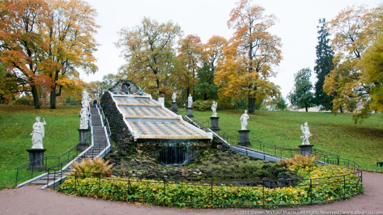 Broad checkerboard cascade climbing a grassy slope, lined with classical statues and topped by a grotto.