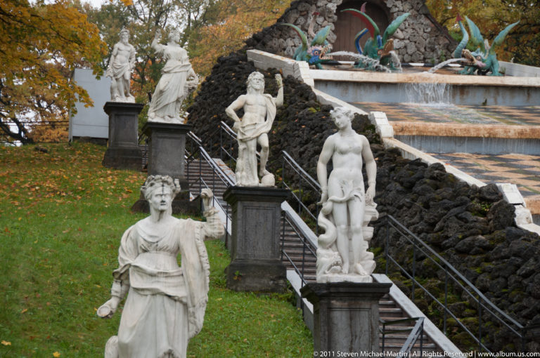 Several classical statues on dark pedestals beside the sloping Chessboard Hill Cascade and dragon fountain.