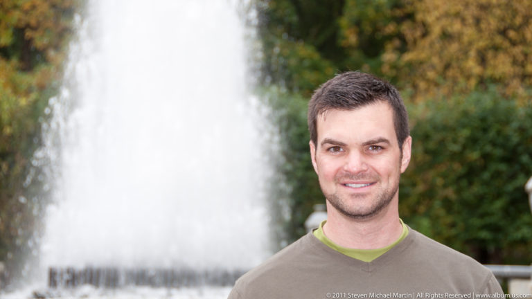 Close portrait of a dark-haired visitor with a large white fountain jet blurred behind him.