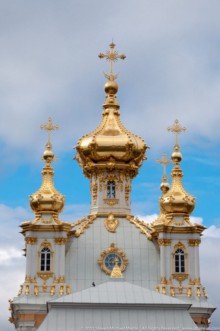 Three ornate gilded cupolas with crosses and gold trim rising above a pale palace roofline.