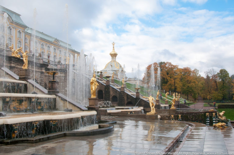 Lower Grand Cascade terraces with gilded statues, wet paving, palace façade, and fountain spray.