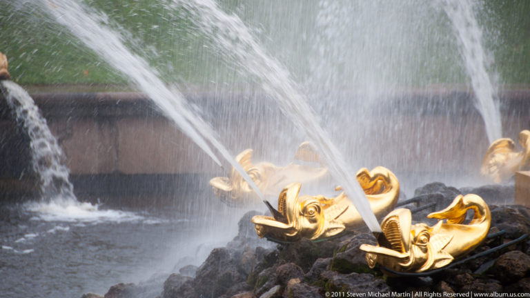 Gilded fish-shaped fountain spouts sending narrow streams across dark wet rockwork.