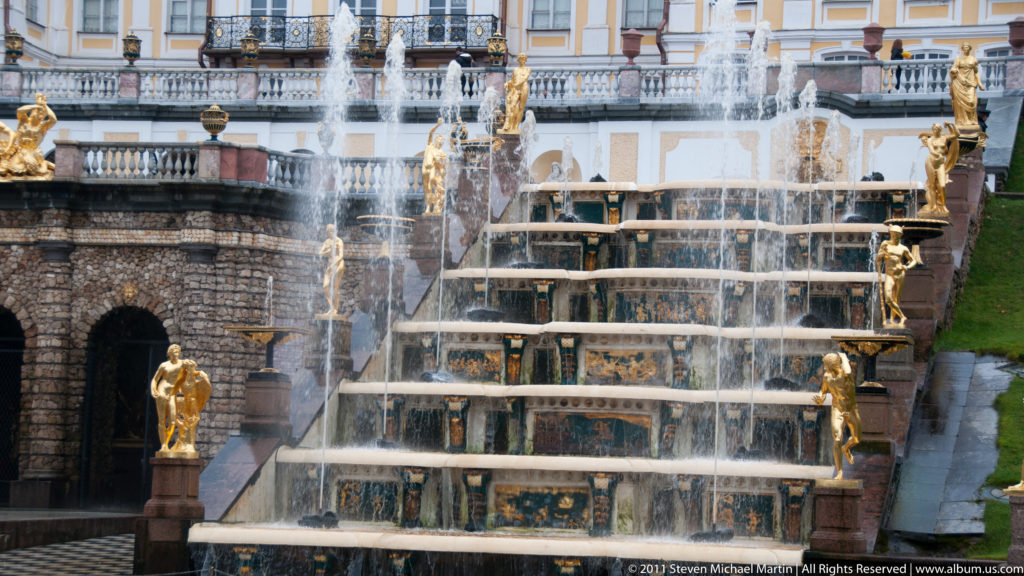 Stepped Grand Cascade with flowing water, dark grotto openings, and gilded statues on pedestals.