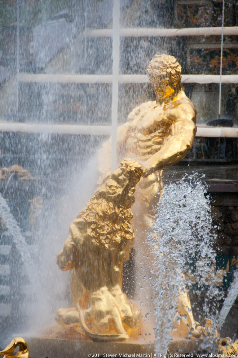 Reclining gilded male fountain figure partly obscured by dense spray and crossing water jets.