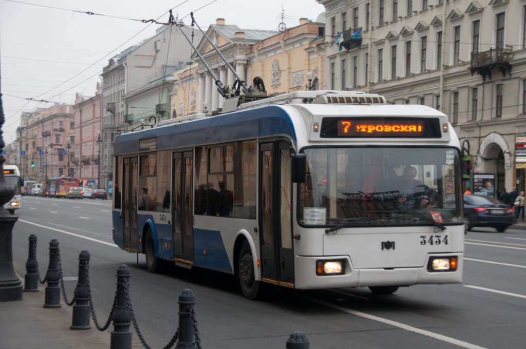 Blue-and-white route 7 trolleybus driving beneath overhead wires on a historic St. Petersburg avenue.