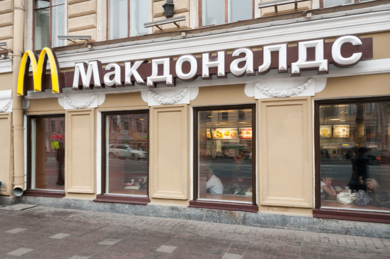 McDonald’s storefront with golden arches and large Cyrillic “Макдоналдс” sign in a historic St. Petersburg building.