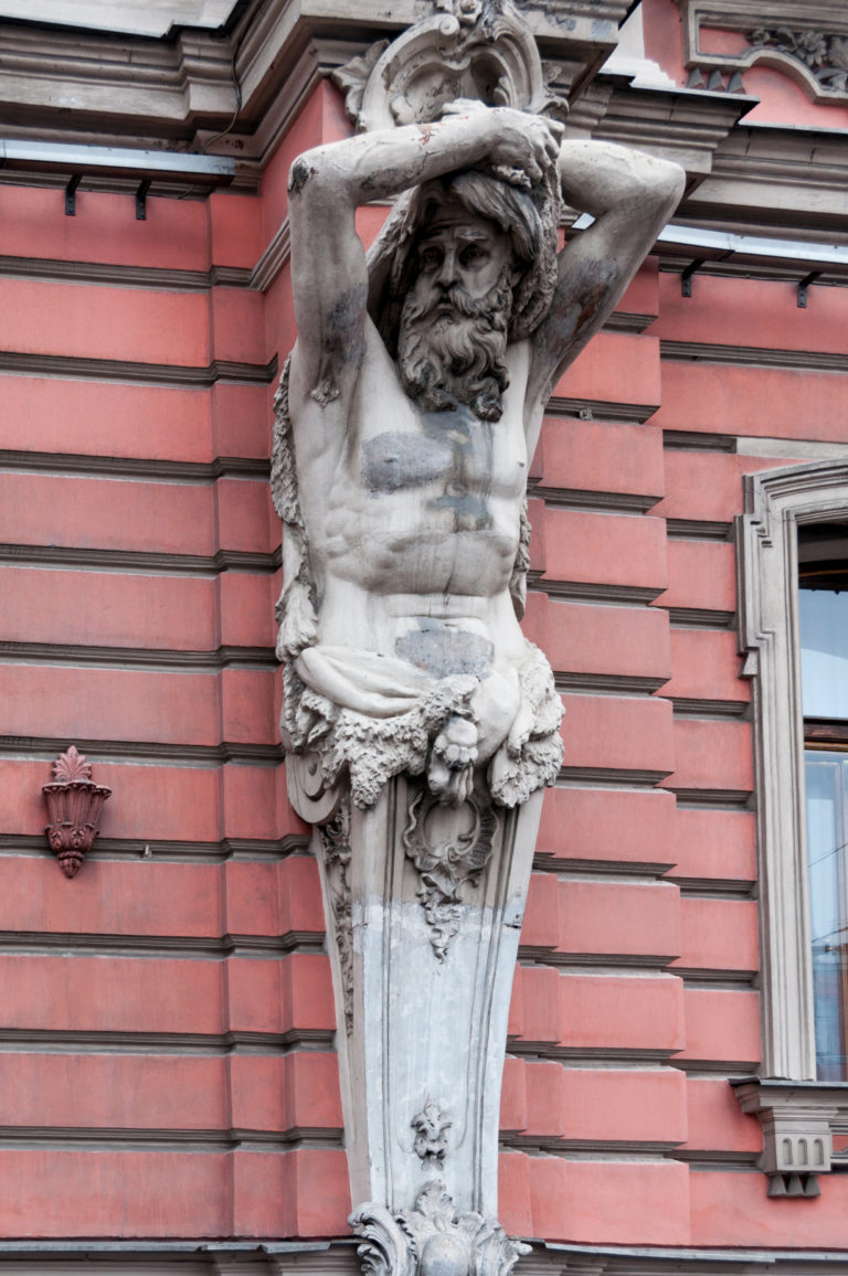 Bearded stone Atlas figure with raised arms supporting a cornice on an ornate pink historic façade.