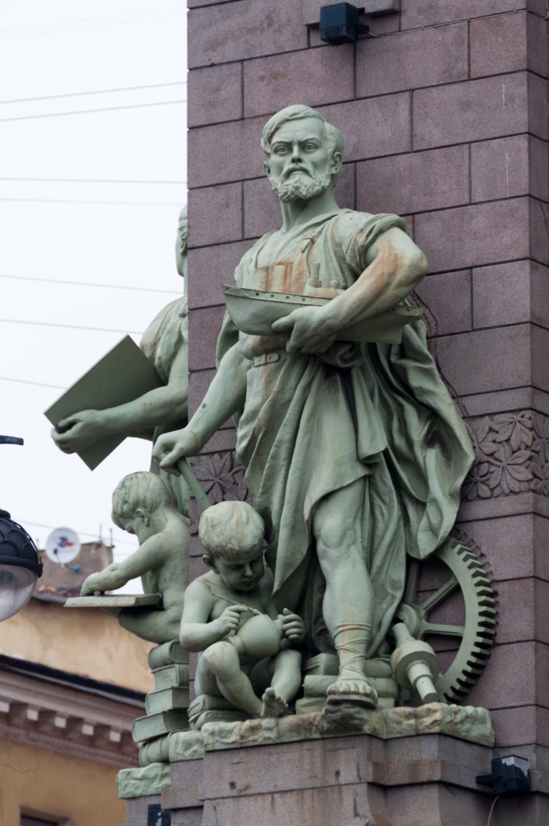 Green-patinated allegorical male figure with drapery and accompanying sculptural attributes on the Eliseyev Emporium façade.