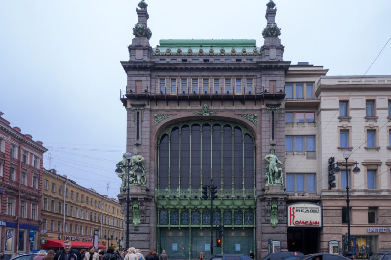 Eliseyev Emporium façade with giant arched window, dark stone frame, green metalwork, and sculptural figures.