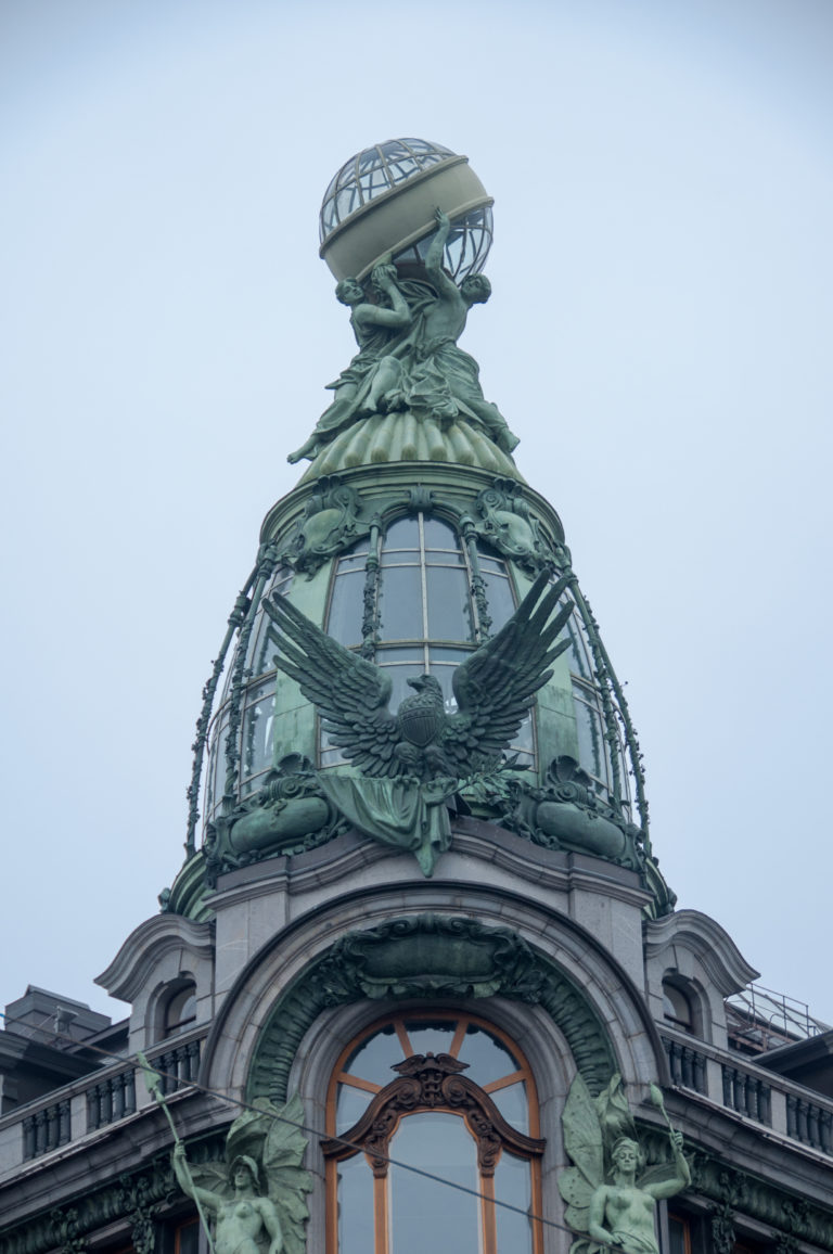 Close view of the Singer House corner tower with green-patinated sculpture, spread-winged eagle, and metal-framed glass globe.