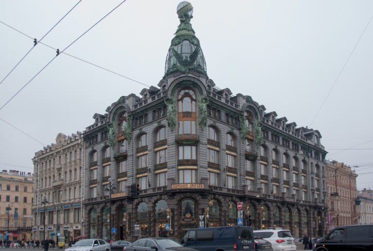Ornate Singer House corner façade with bay windows, green-patinated sculpture, and rooftop glass globe above busy traffic.