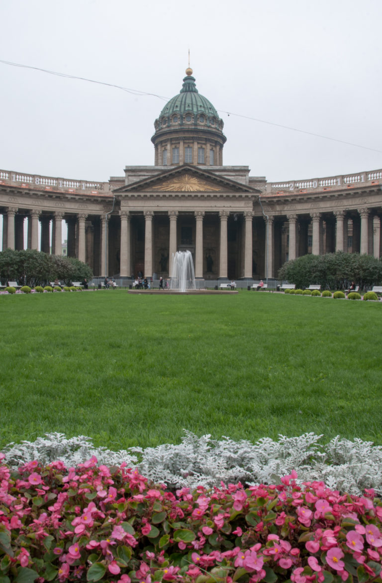 Kazan Cathedral behind a green lawn and flowerbeds, with fountain, portico, colonnade, and green dome centered.