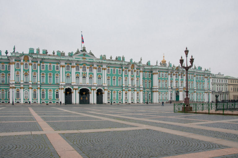 Wide Palace Square with patterned cobblestones and the long green-and-white Winter Palace façade beyond.