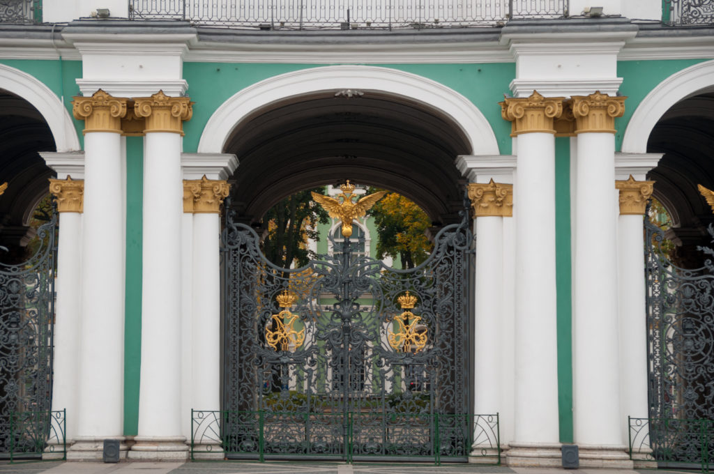 Black wrought-iron Winter Palace gate with gilded imperial eagles framed by white columns and green walls.