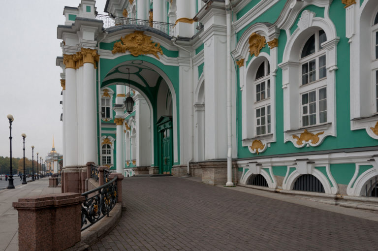 Green-and-white Winter Palace façade with tall windows and gilded ornament beside a deep arched gateway.