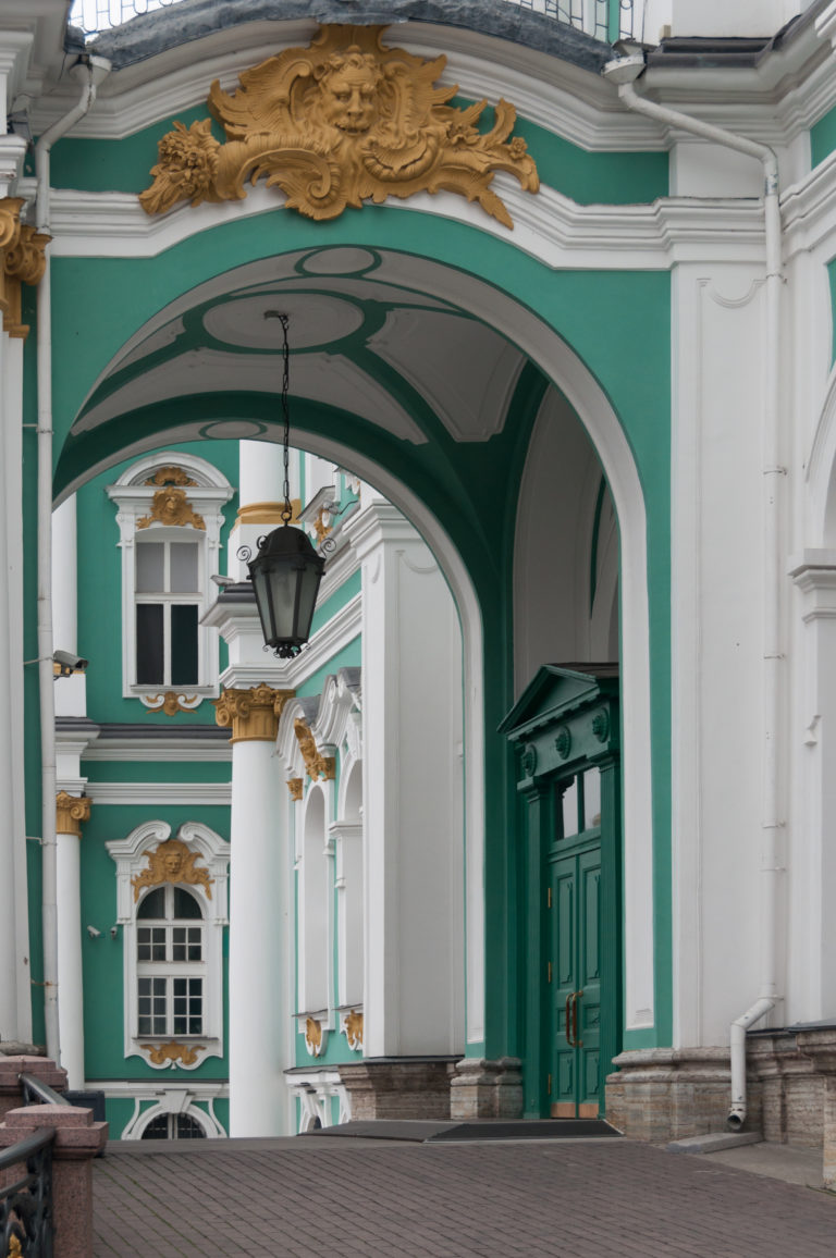 Arched Winter Palace passage with hanging lantern, white columns, gilded capitals, and green doors beyond.