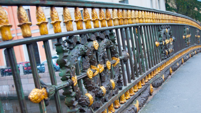 Curving dark cast-iron bridge railing decorated with gilded leaves, rosettes, and relief ornament.