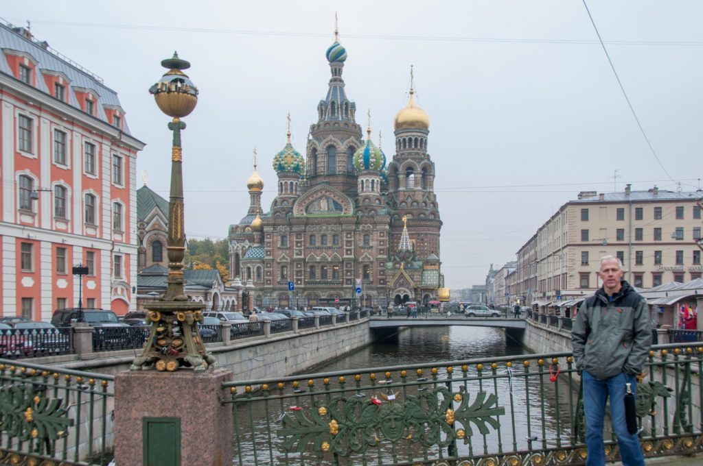 Church of the Savior on Spilled Blood beyond the Griboyedov Canal, with ornate railing and a visitor in the foreground.