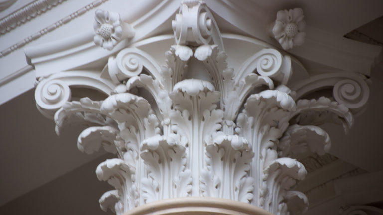 Close-up of a white Corinthian column capital carved with acanthus leaves, volutes, and floral ornament.