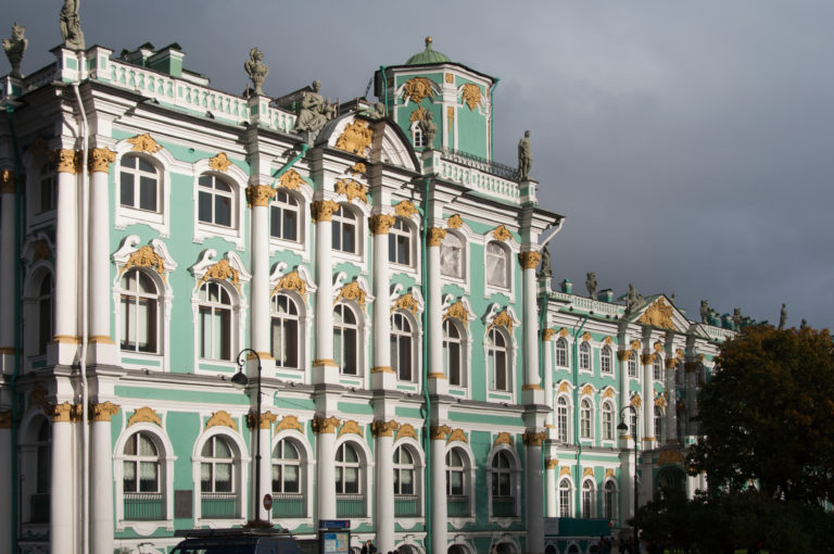 Oblique view along the green-and-white Winter Palace façade with gilded Baroque ornament and rooftop statues.
