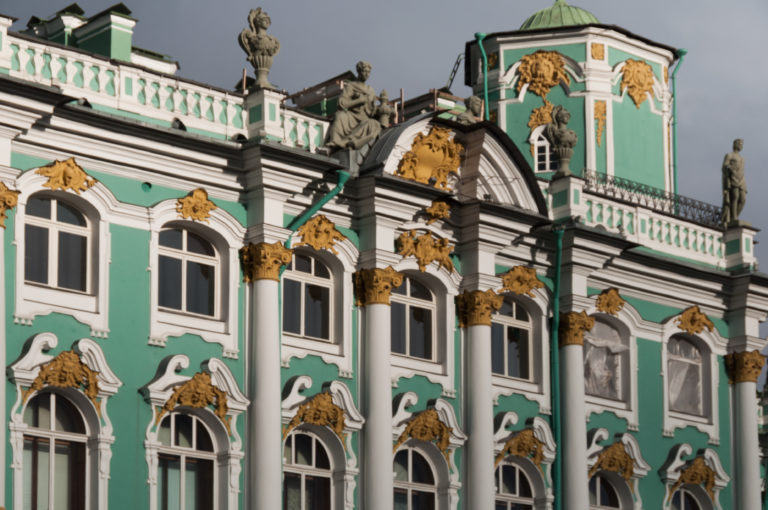 Close view of the green-and-white Winter Palace façade with gilded capitals, arched windows, and roofline statues.