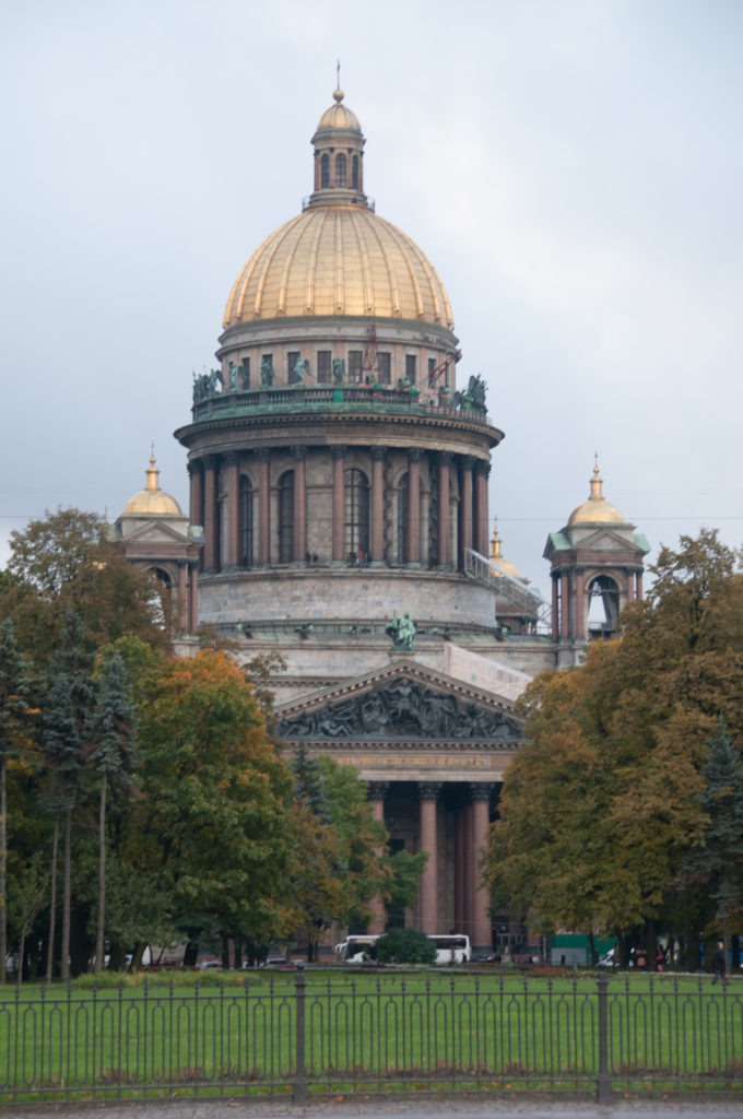 Large gilded dome of St. Isaac’s Cathedral above columns and autumn trees, with smaller cupolas at either side.