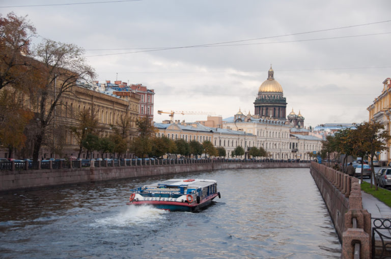 Tour boat traveling along a stone embankment canal toward the distant gilded dome of St. Isaac’s Cathedral.