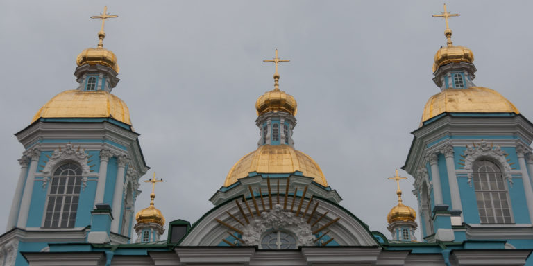 Three gilded domes and crosses above the turquoise-and-white Baroque façade of St. Nicholas Naval Cathedral.