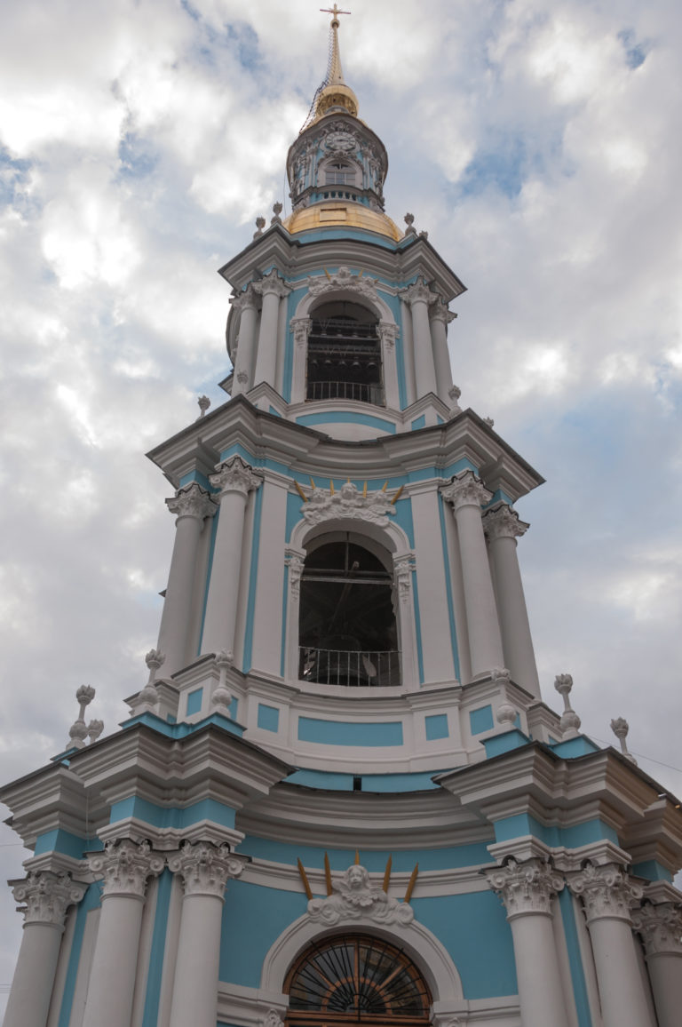 Blue-and-white Baroque bell tower with stacked arched openings, white columns, gilded details, and a small cupola.
