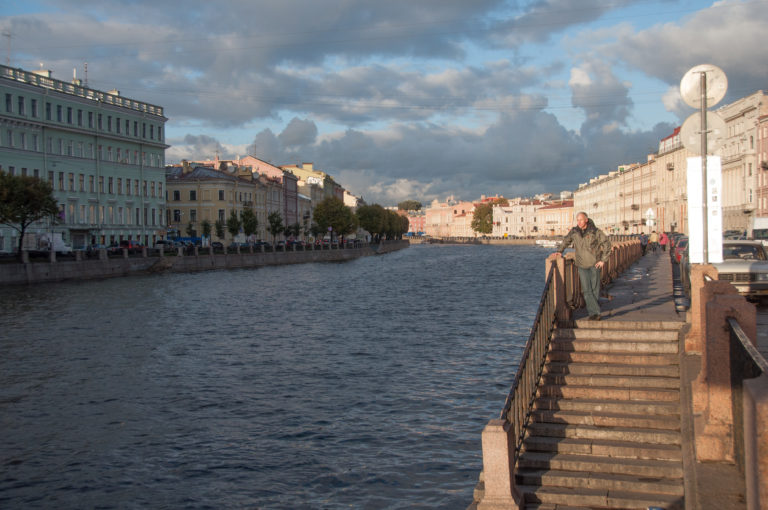 Stone steps and pedestrians beside the Fontanka River, with pastel historic buildings lining the opposite embankment.