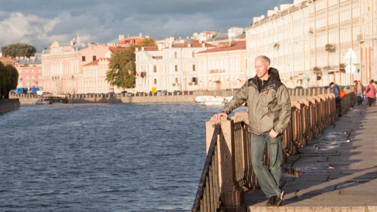 Man leaning on the Fontanka River railing with sunlit pastel historic buildings stretching along the opposite bank.