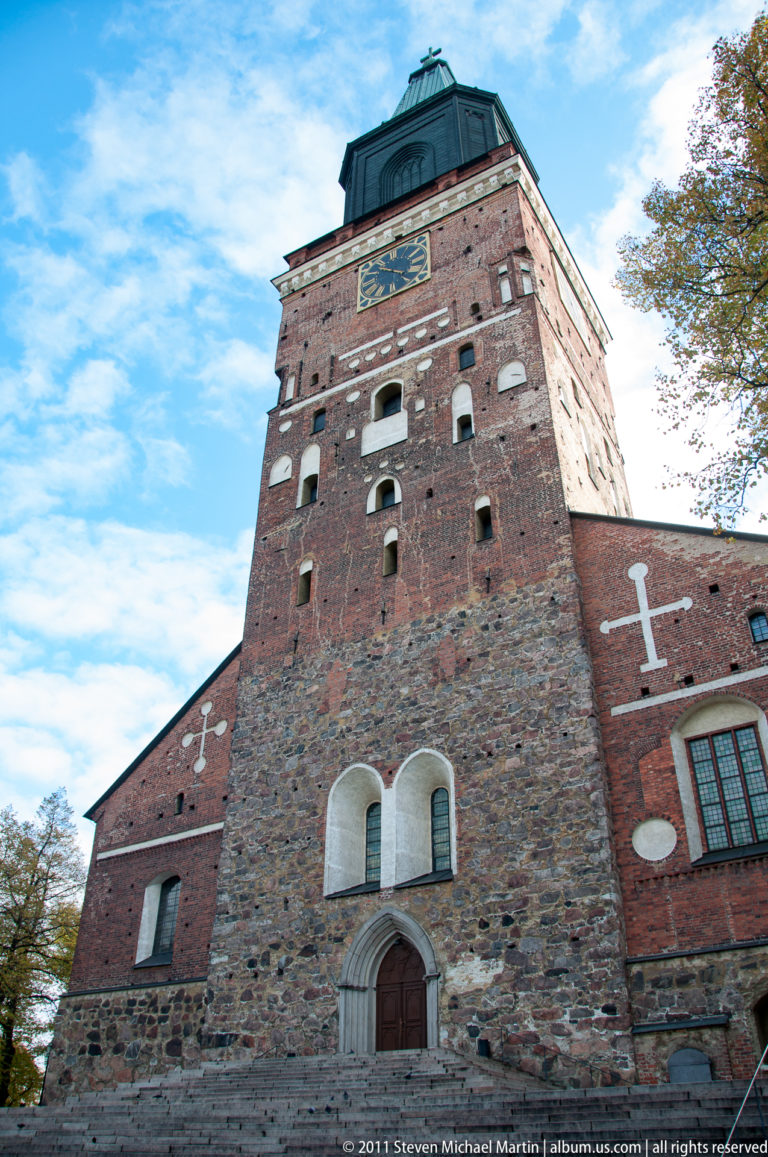 Low-angle view of Turku Castle entrance tower with rough stone and brick walls, small openings, arched doorway, and green roof