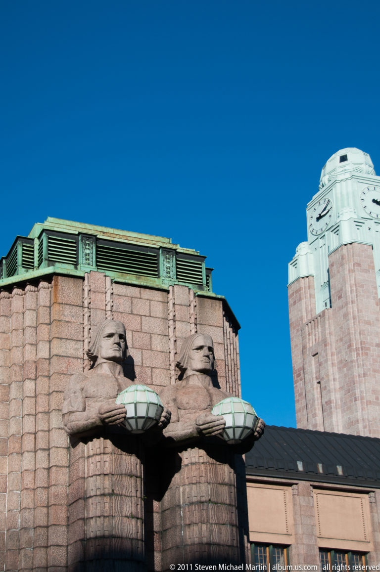 Granite lamp-bearer statues on Helsinki Central Railway Station at left with the tall clock tower rising at right