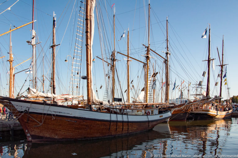 Wooden tall ship moored in Helsinki harbor with tall masts, dense rigging, bowsprit, and other sailing vessels behind