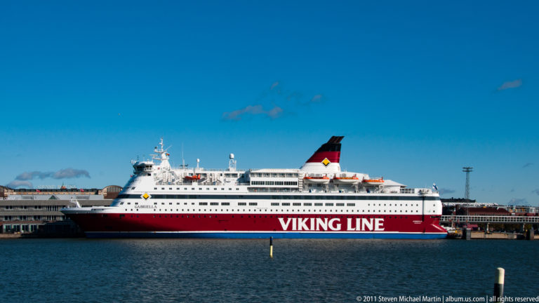 Red-and-white Viking Line passenger ferry broadside in Helsinki harbor, with rows of windows, lifeboats, and a black-and-red funnel.