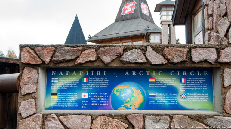 Multilingual Napapiiri–Arctic Circle information panel and polar map mounted in a rough stone wall.