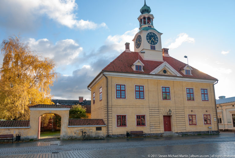 Front view of Old Rauma Town Hall with ochre walls, red-trimmed windows, red roof, white clock tower, and arched side gateway.