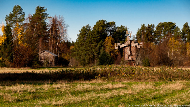 Small wooden windmill with four open-framed sails beside autumn woodland and a grassy field near Rauma.