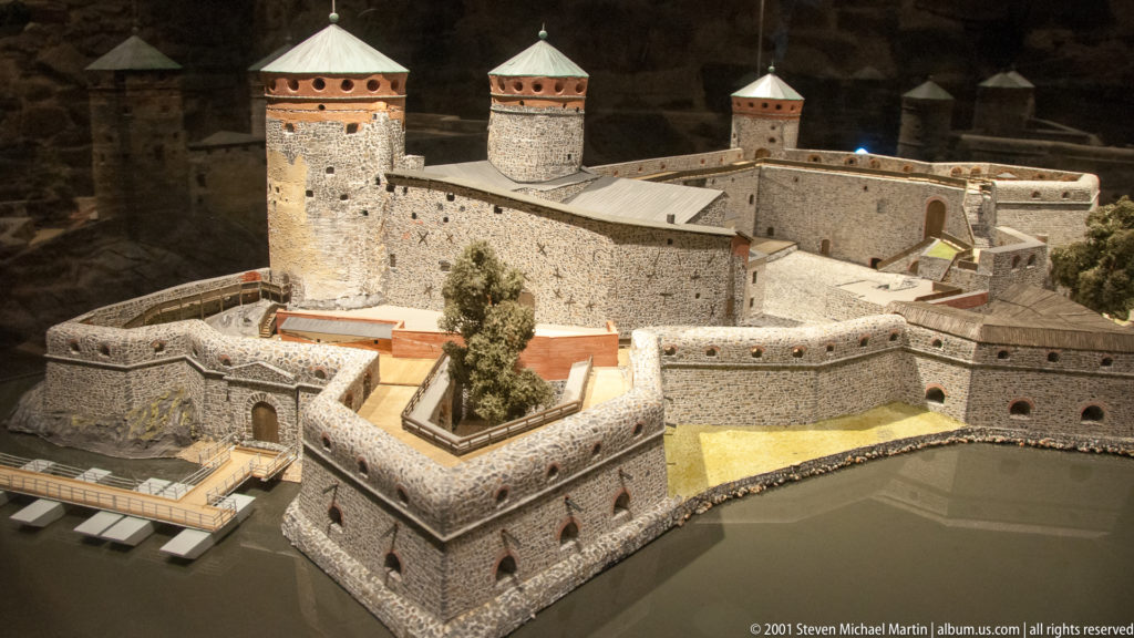 Scale model of Olavinlinna Castle showing round towers, curtain walls, inner buildings, outer works, and surrounding water.