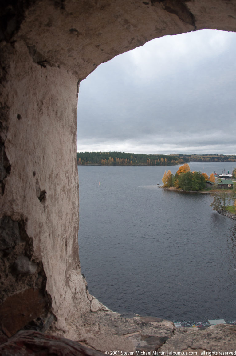 Wide lake and wooded islands seen through a deep rough-edged opening in Olavinlinna Castle.