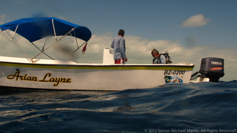 Dive boat Arian Layne on the water with two people aboard and an outboard motor at the stern.