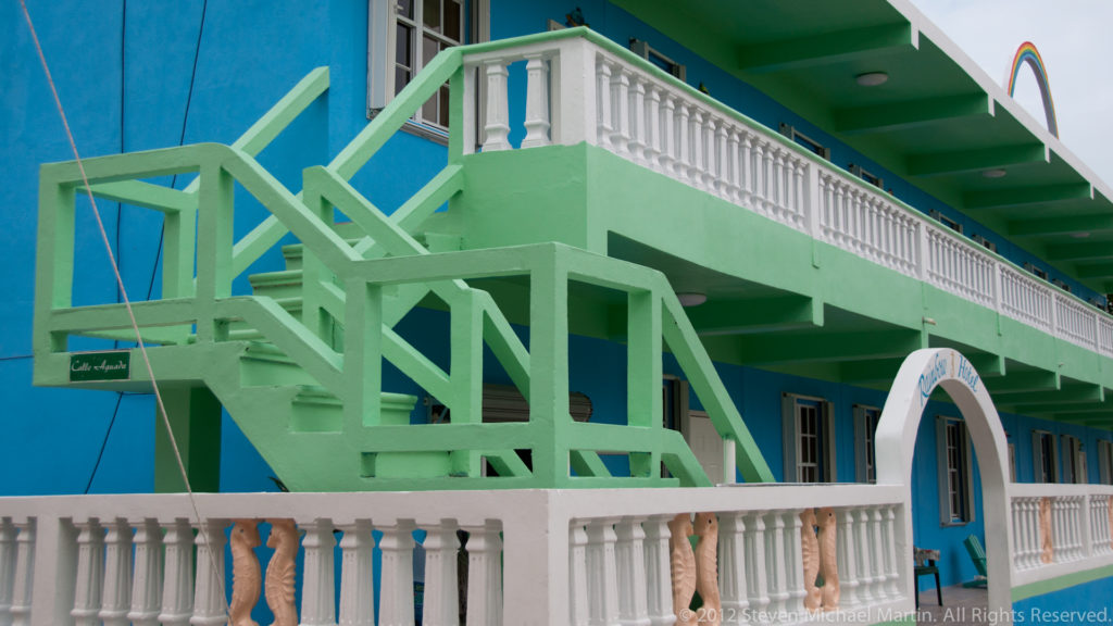Bright green exterior staircase and white balustrades against a turquoise two-story building on Caye Caulker.