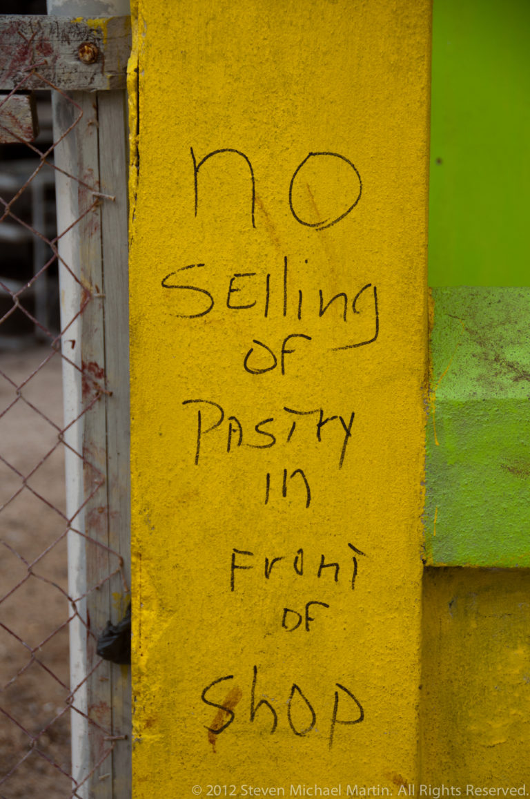 Handwritten words “no selling of pastry in front of shop” on a yellow wall beside a bright green painted section.