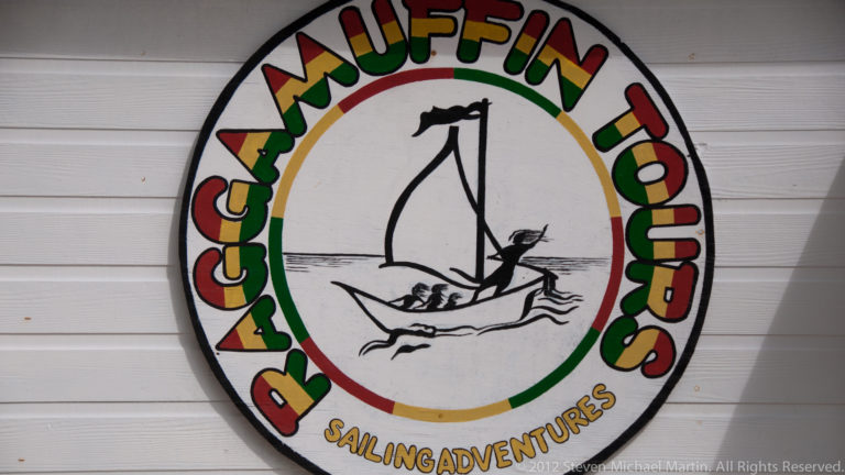 Round Raggamuffin Tours Sailing Adventures sign with colorful lettering and a central drawing of a small sailboat.