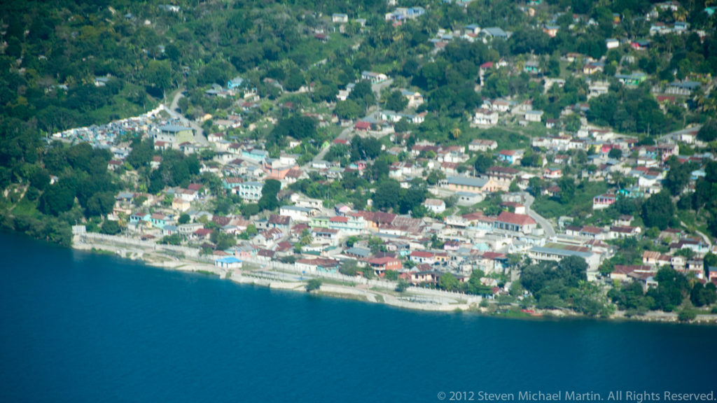 Lakeside neighborhood of Flores with tightly grouped pastel and white buildings rising behind the blue water of Lake Petén Itzá.