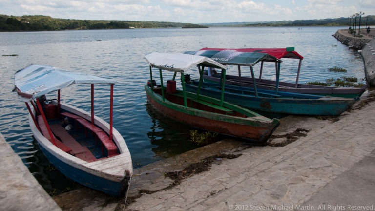 Three narrow covered passenger boats moored beside the stone waterfront on Lake Petén Itzá in Flores, Guatemala.